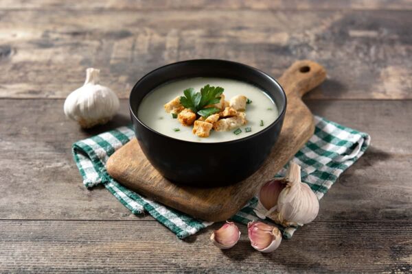red garlic soup topped with croutons in black bowl on wooden table magefesa